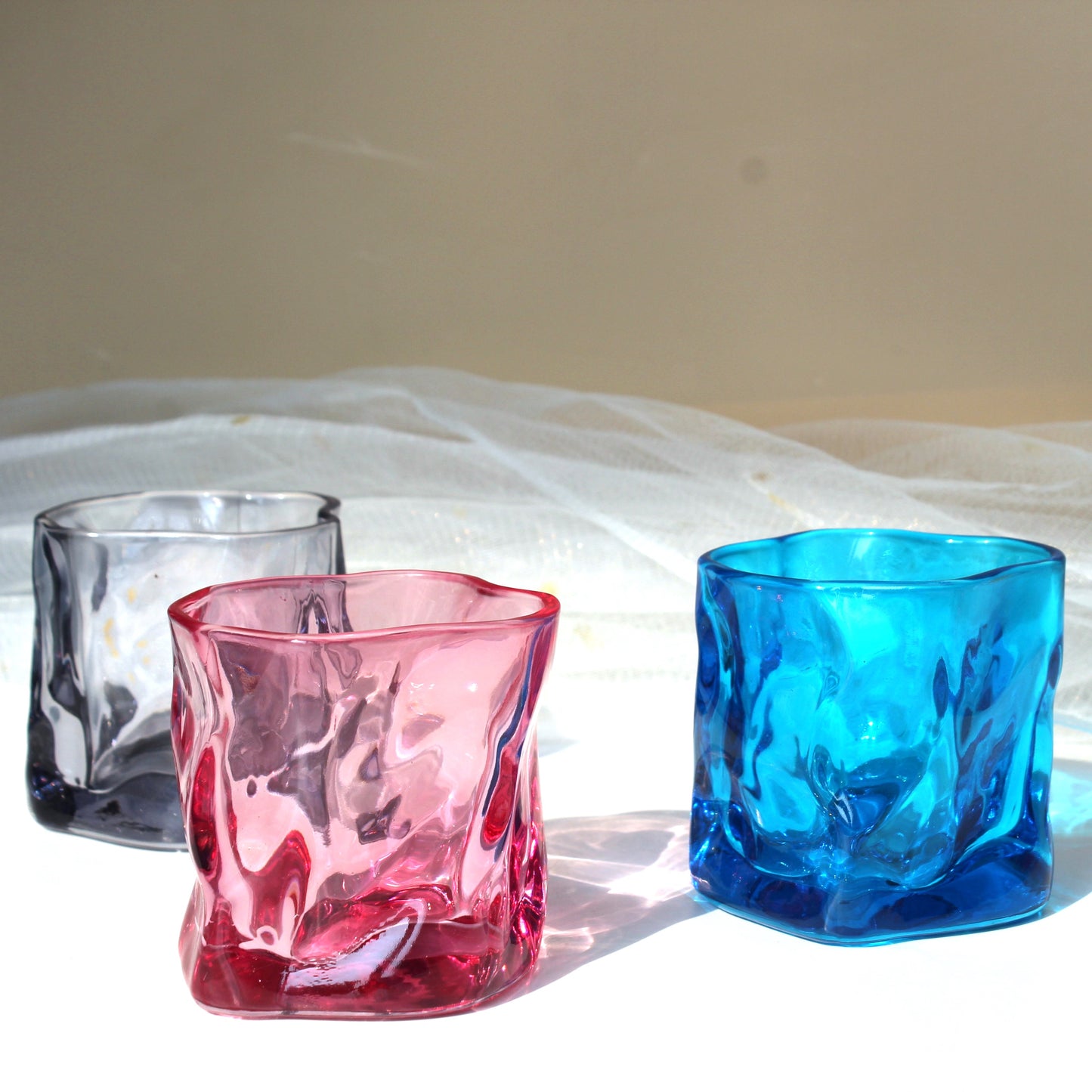 Three colorful glass tumblers on a white fabric background
