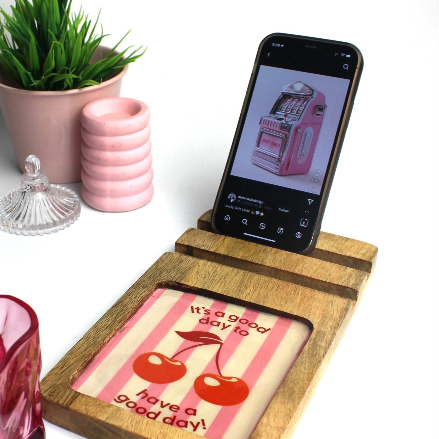 Phone stand with a cute print, pink glass, and plant on a white surface