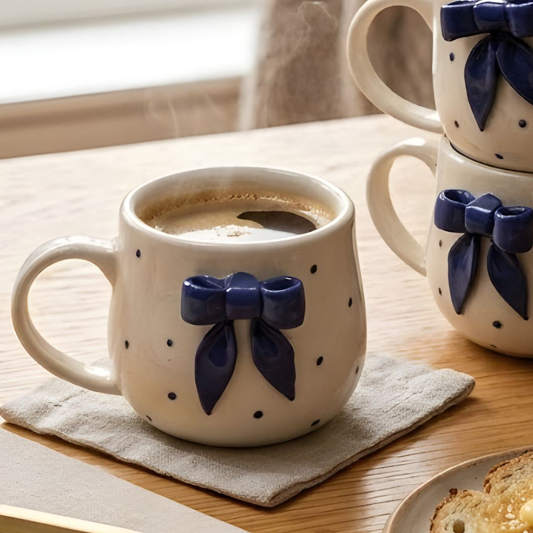 Ceramic mug with blue bow design on a wooden table with a book and toast.