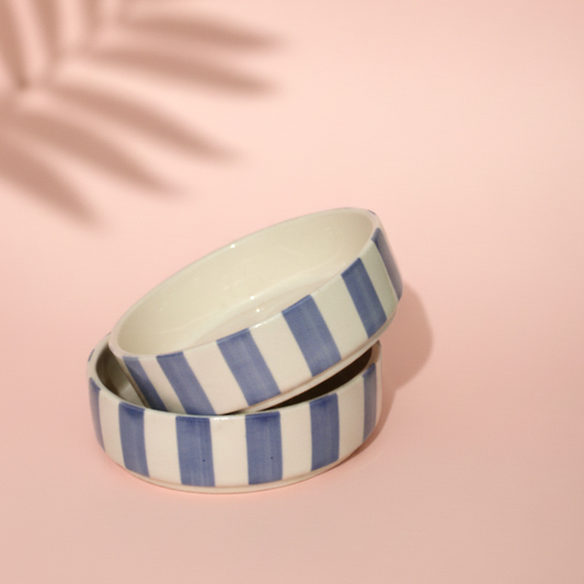 Set of two ceramic bowls with blue and white stripes on a pink background