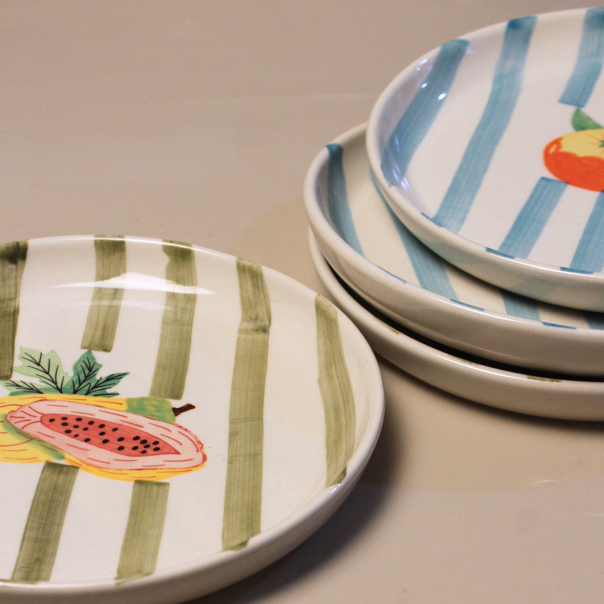 Set of ceramic plates with fruit designs on a beige surface