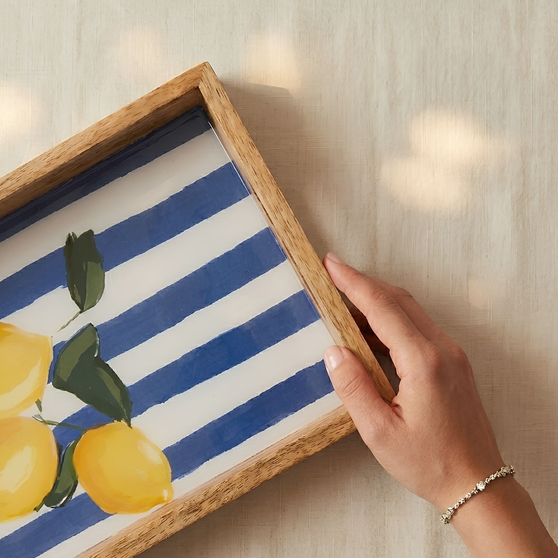 Hand holding a framed artwork with blue and white stripes and lemons.