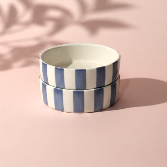 Two ceramic bowls with blue and white stripes on a pink background