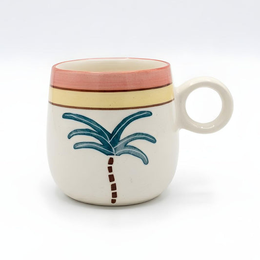 A white ceramic mug with a handle, decorated with a blue palm tree motif and horizontal stripes in terracotta and yellow on the rim, set against a plain white background.