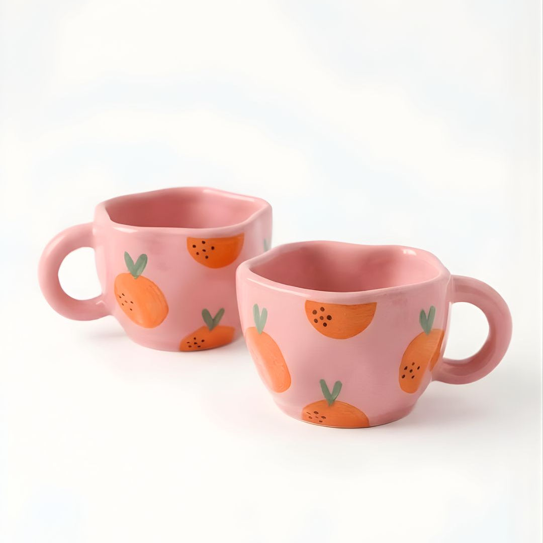 Two pink mugs with orange and green pattern on a white background