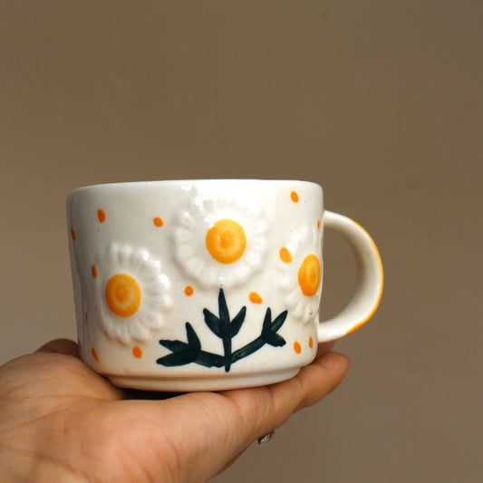 White mug with floral design held by a hand against a plain background
