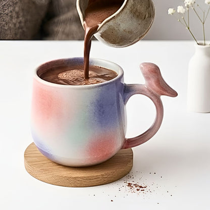 Person pouring hot chocolate into a tie-dye mug with a wooden coaster on a white surface.