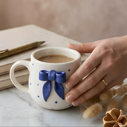 Person holding a mug with a blue bow design on a marble surface.