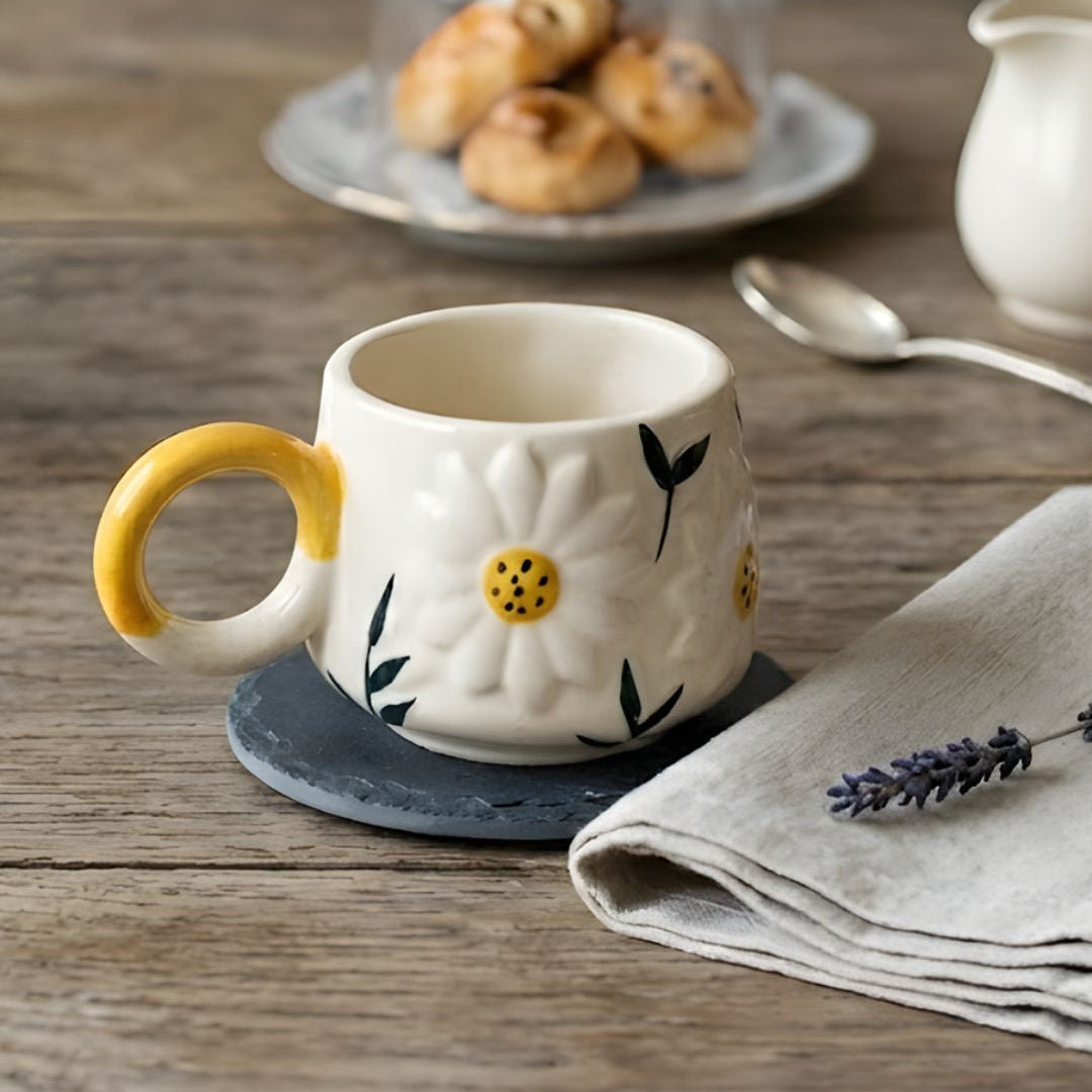 Decorative mug with floral design on a wooden table with pastries and a napkin.