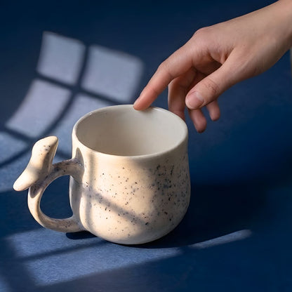 Hand reaching towards a speckled ceramic mug on a dark surface with a window casting shadows.