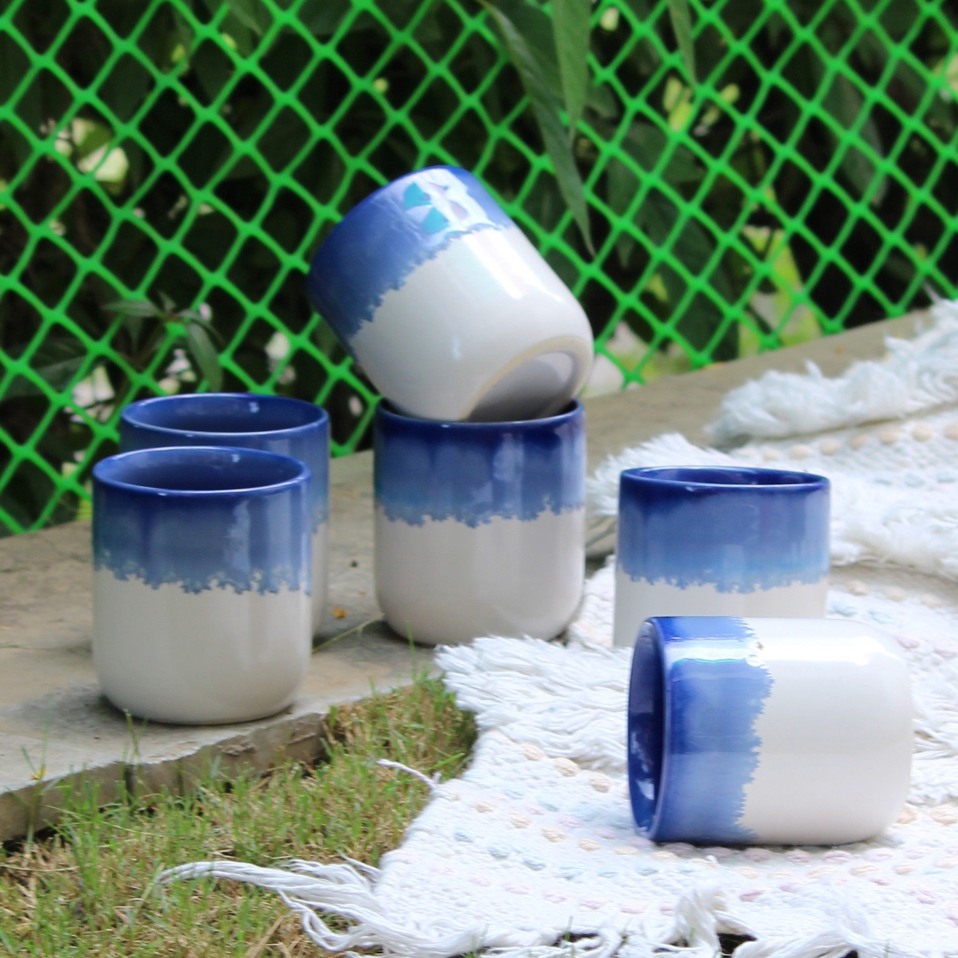 Set of blue and white ceramic cups on a stone surface with a green lattice background