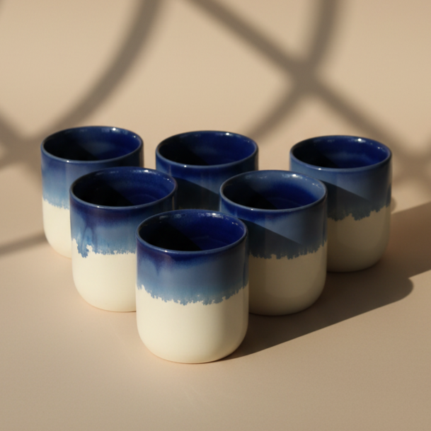 Set of six blue and white ceramic cups on a beige surface with soft shadows.