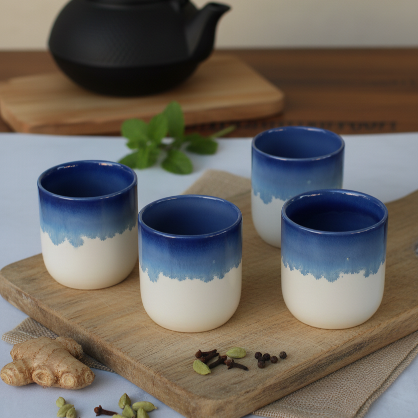 Four blue and white ceramic cups on a wooden board with a teapot in the background.
