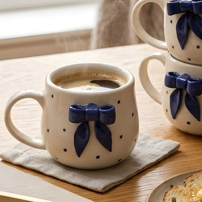 Ceramic mug with blue bow design on a wooden table with a book and toast.