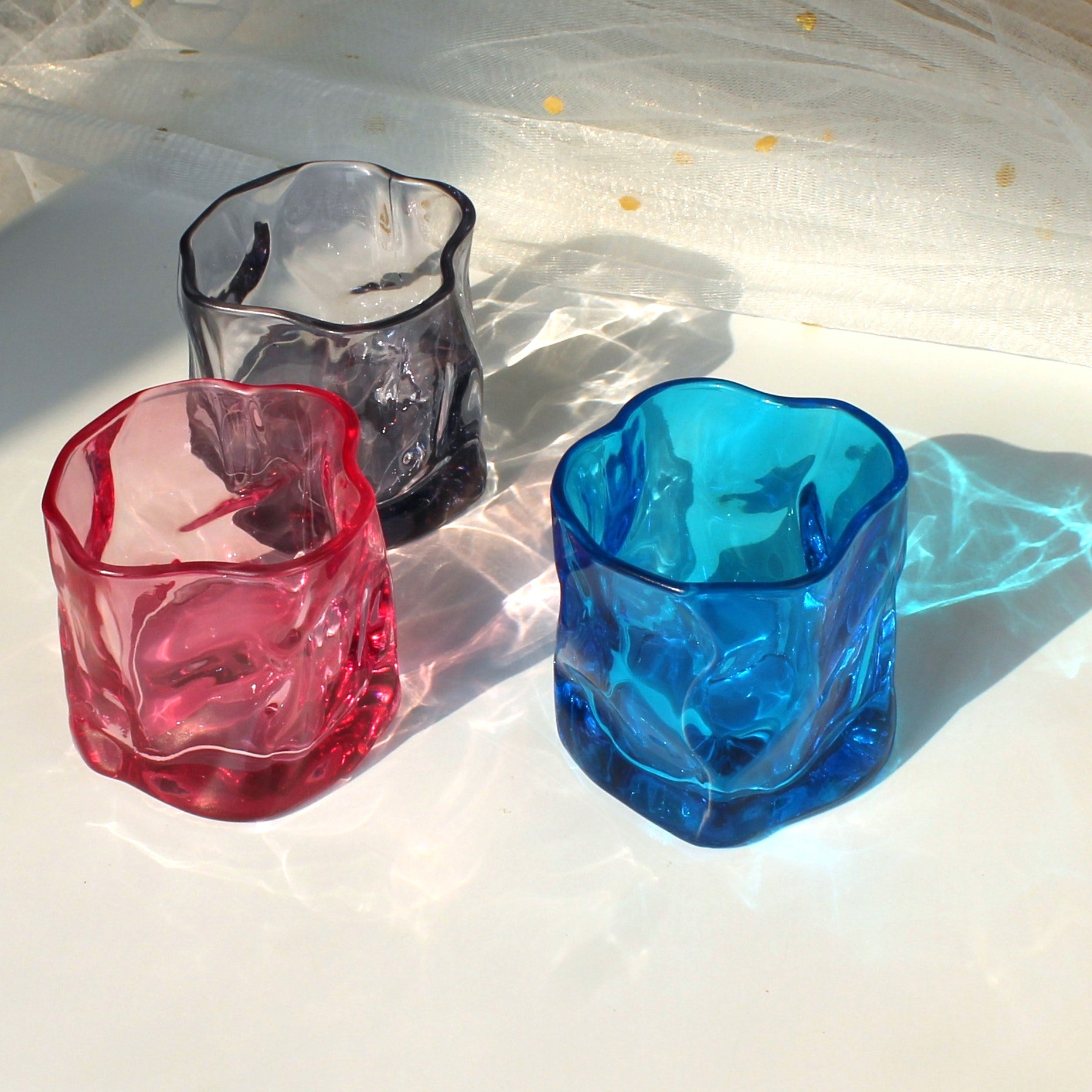 Three colorful glass tumblers on a textured white surface