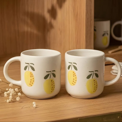 Two white mugs with lemon designs on a wooden surface.