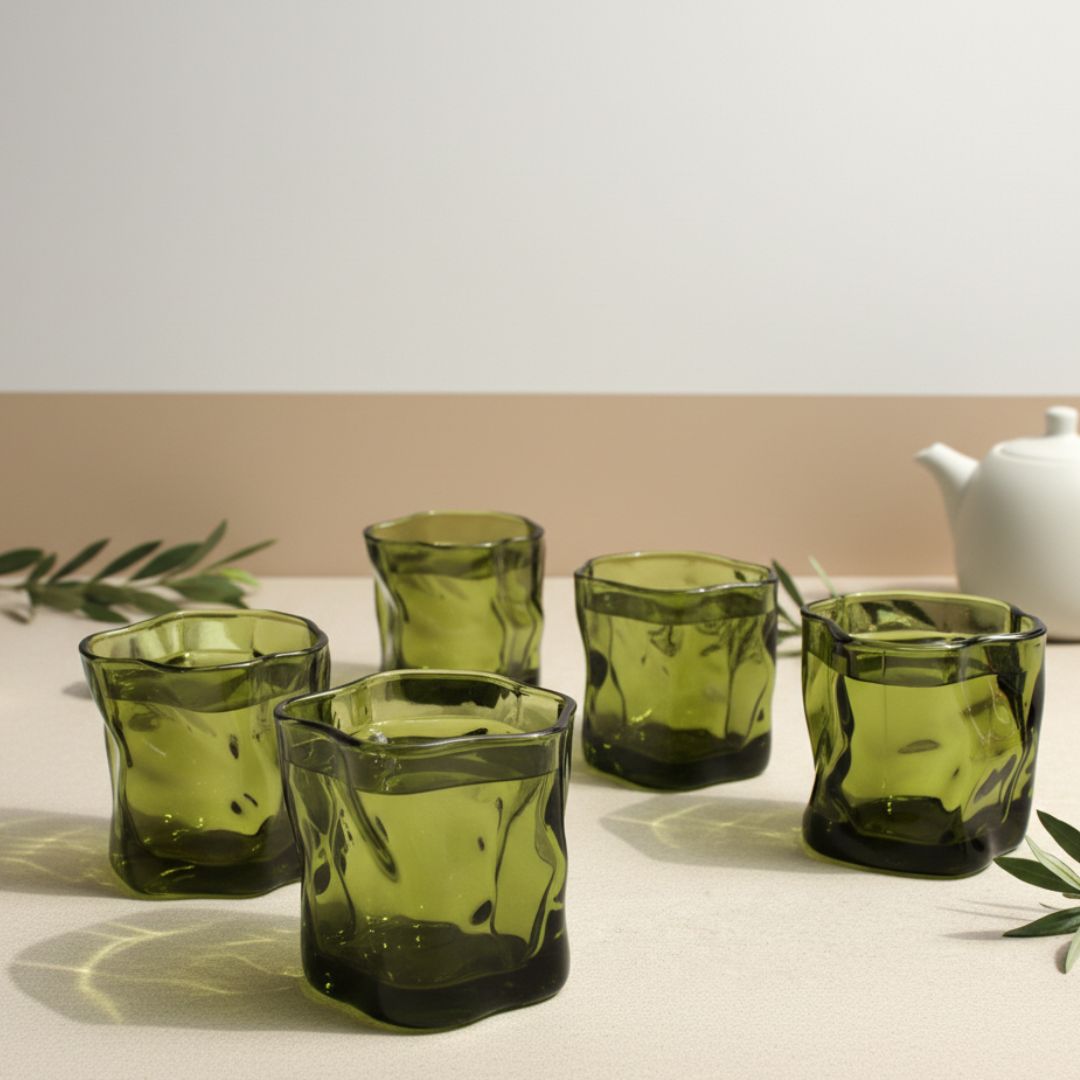Set of six green glass tumblers on a light surface with a white teapot in the background.
