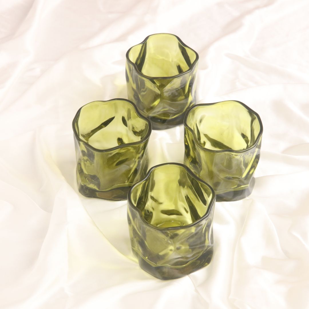 Four green glass tumblers on a white fabric background