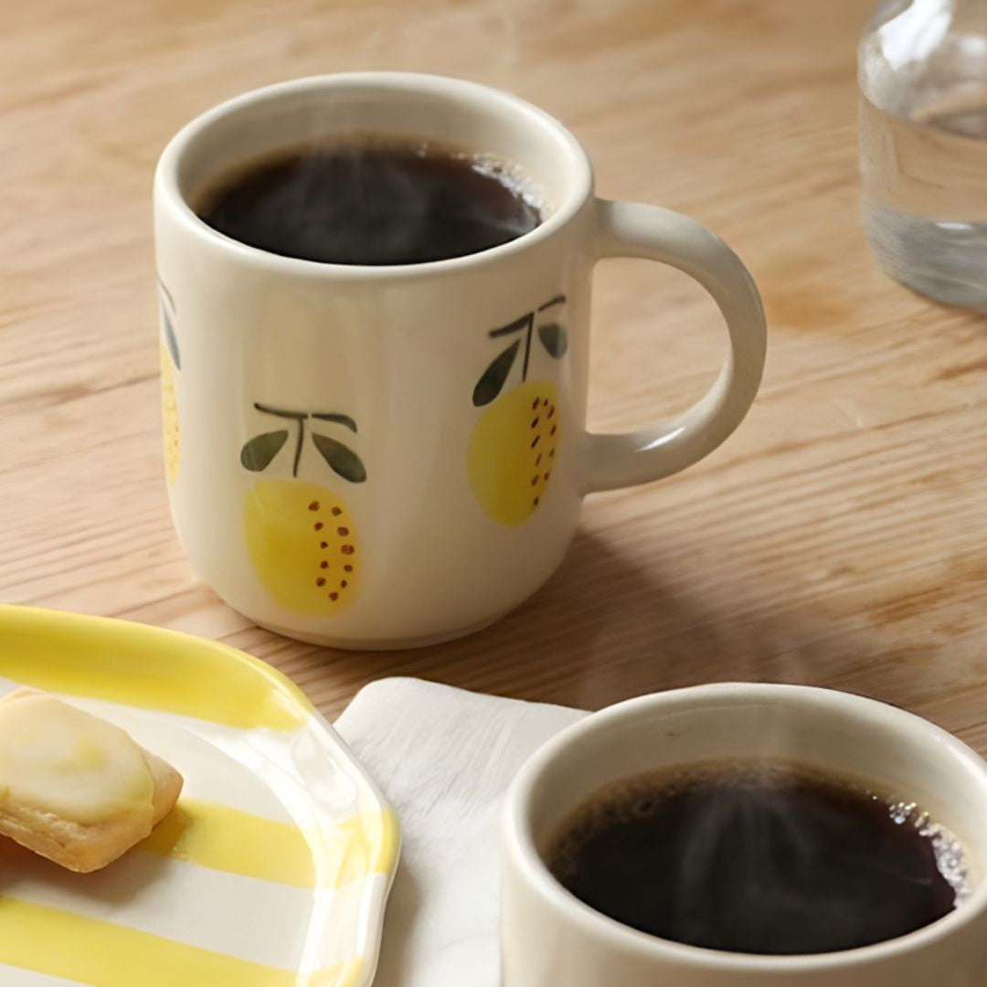 Two mugs of coffee on a wooden table with a plate of pastries.